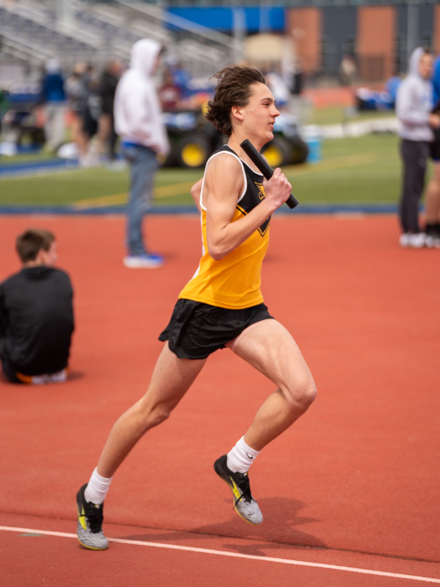 Track athlete in yellow singlet runs with determined form on red track during competition.
