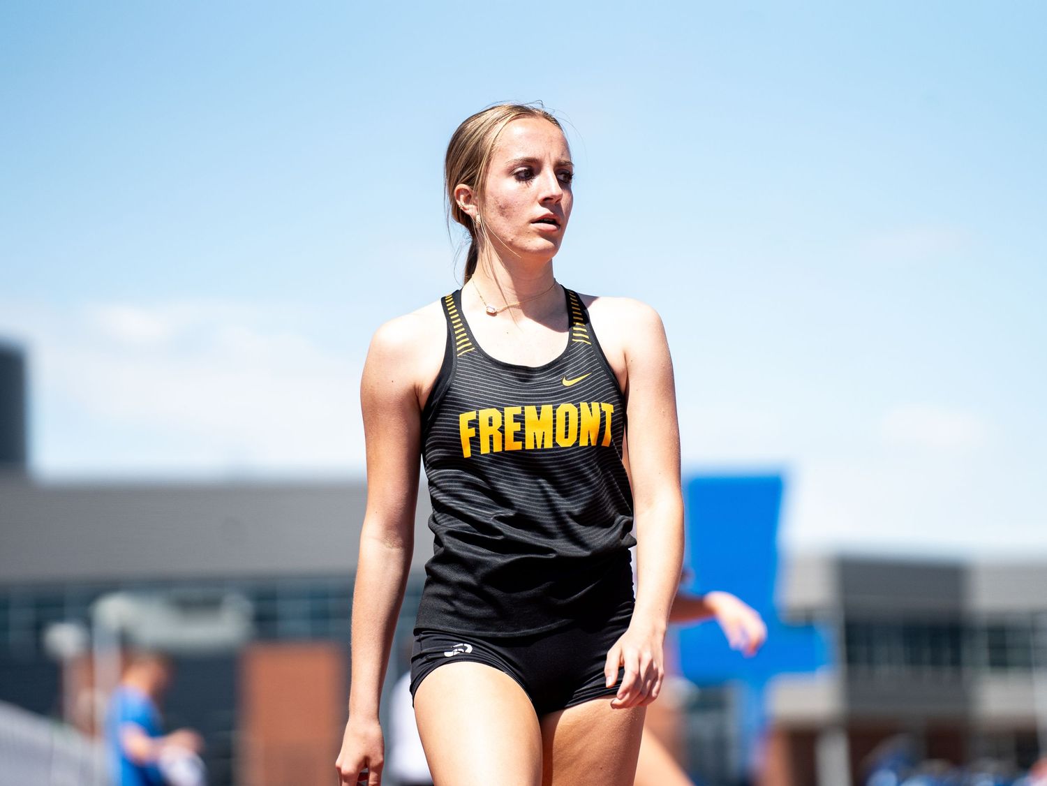 Track athlete in black tank top stands on field during competition.