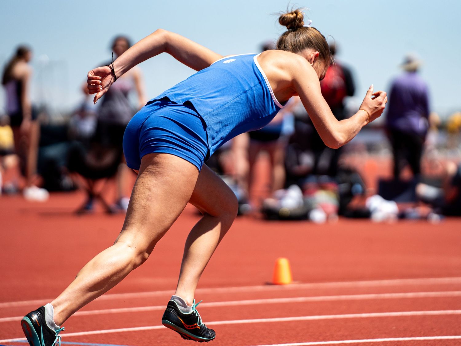 Athlete in blue uniform launches from starting position on red track.