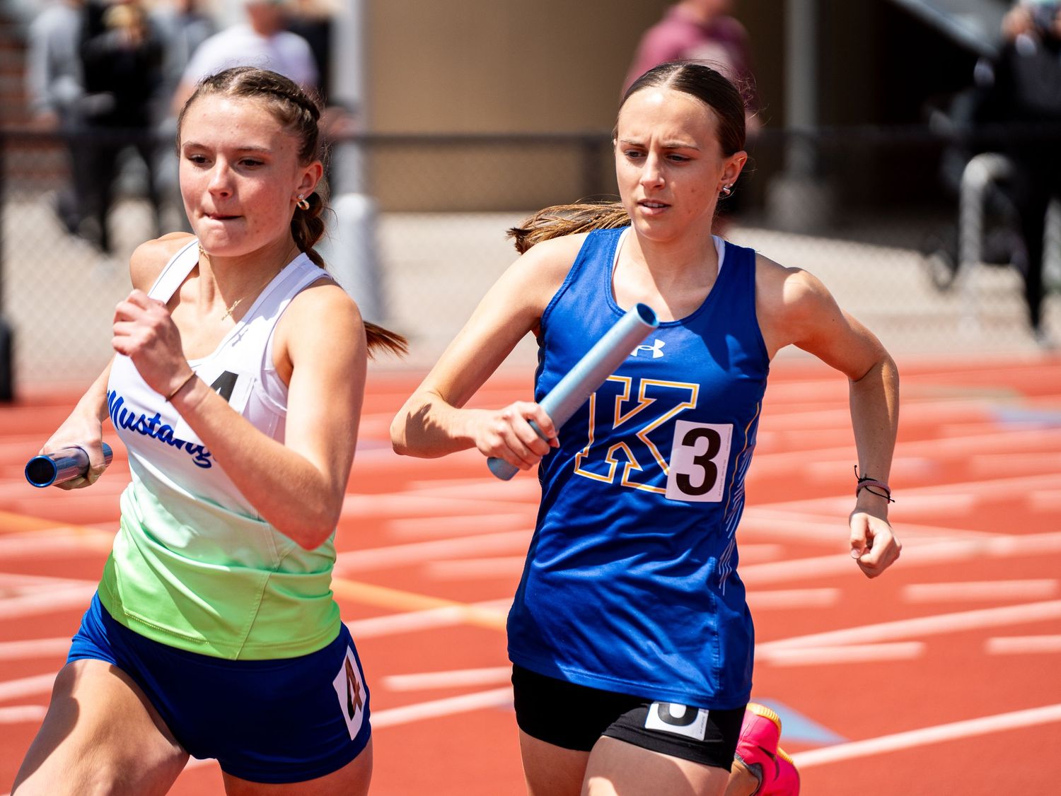 Two athletes sprint neck and neck on a red track during a competitive race.