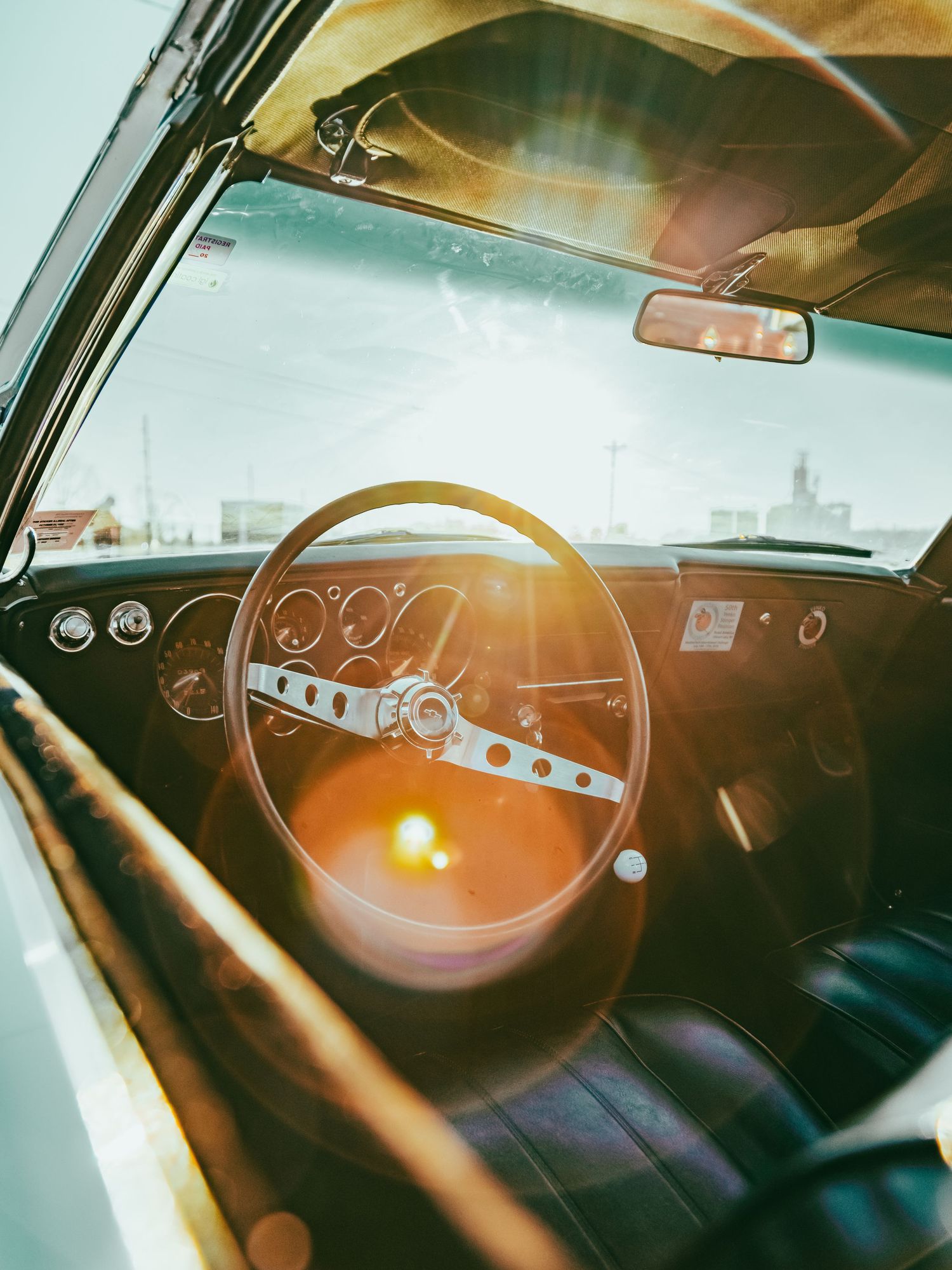 Vintage car dashboard and steering wheel illuminated by warm sunlight through windshield.