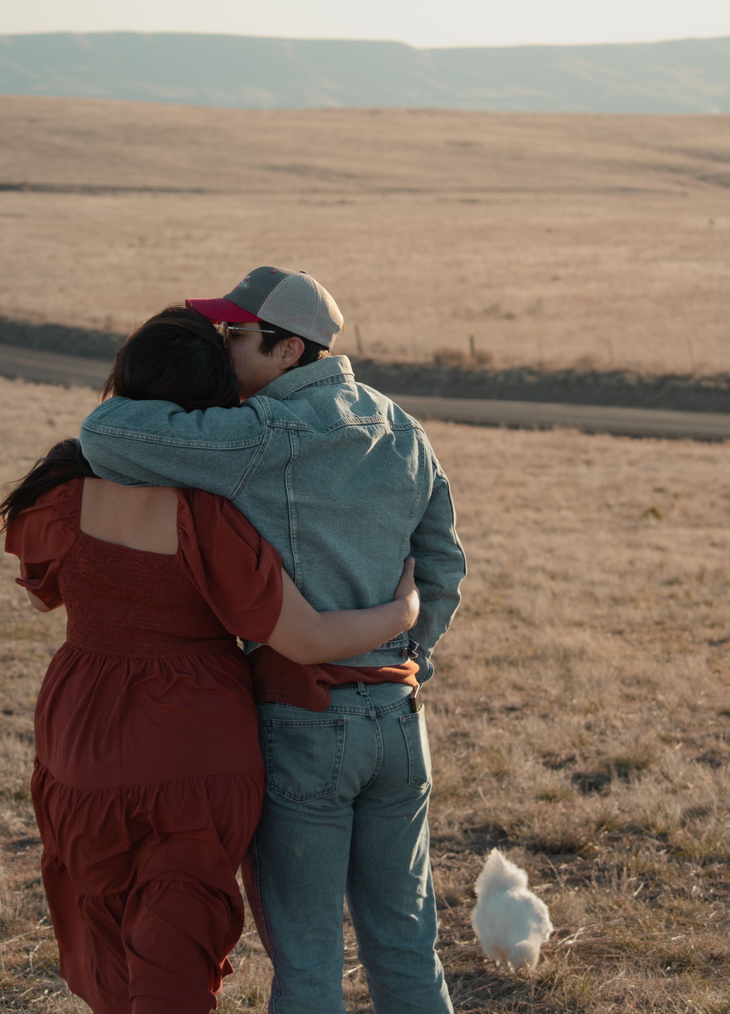 Couple embracing in golden field with their goat beside them during sunset farm session in Pasco WA