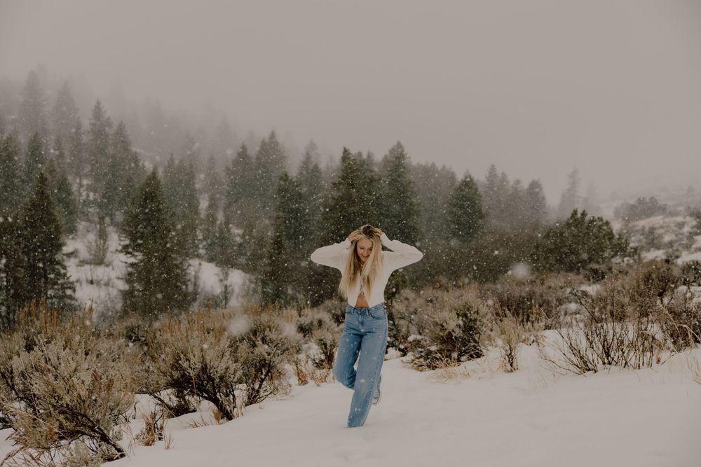 Someone stands in winter landscape with snow covered evergreen trees and foggy mountains in the background.