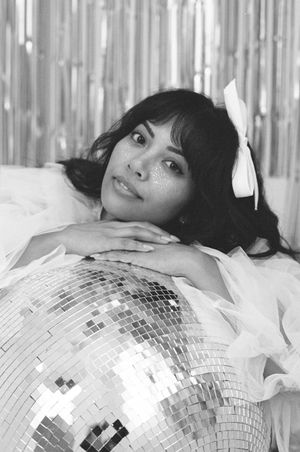 Black and white portrait with disco ball and white bow accessory against metallic backdrop.