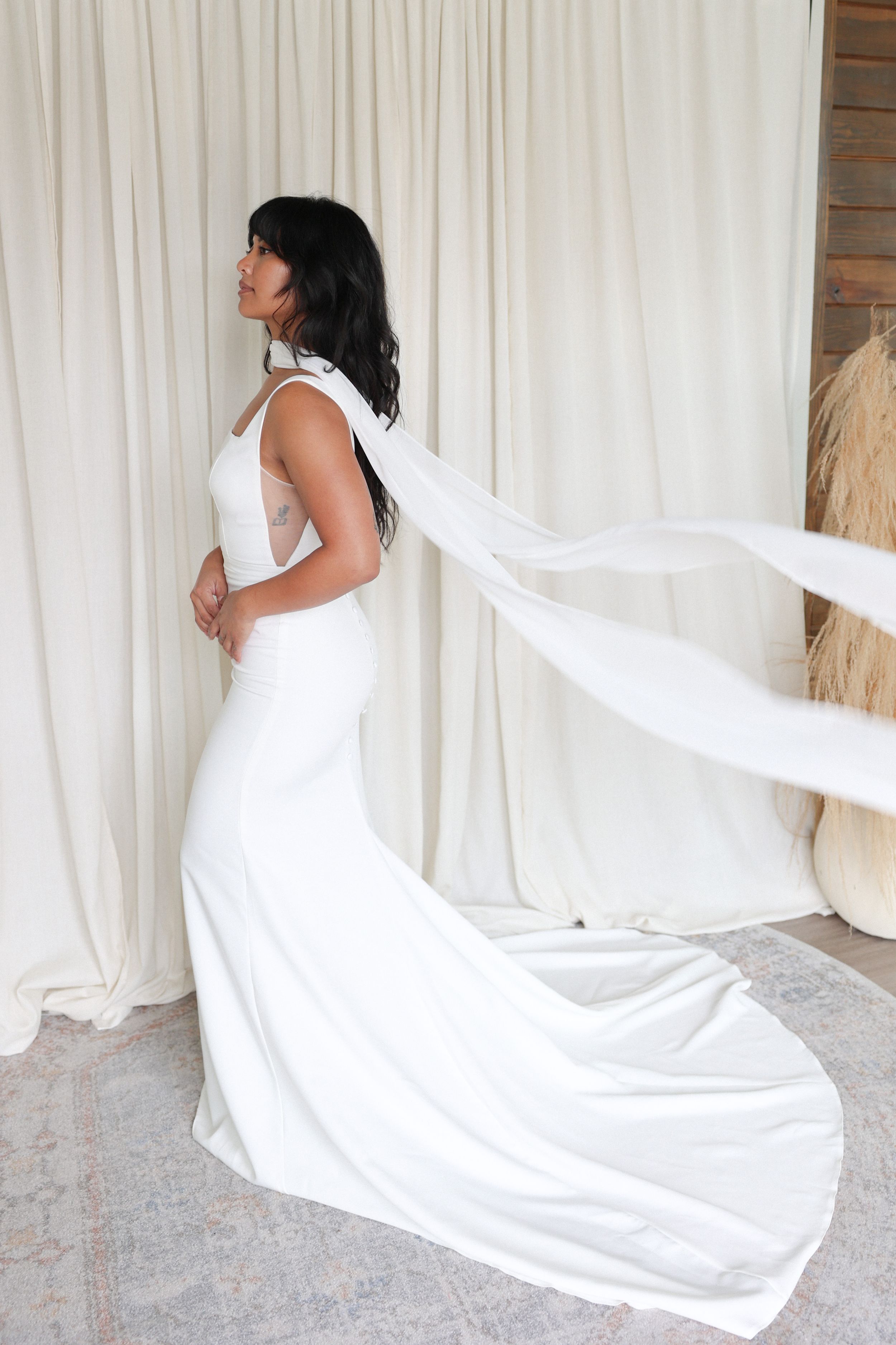An elegant white wedding gown with a flowing train photographed against light curtains.