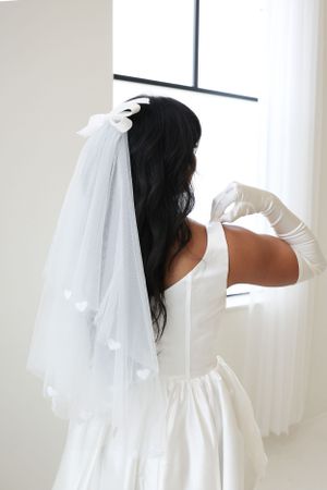Back view of a wedding dress with delicate veil and long white gloves in natural light.