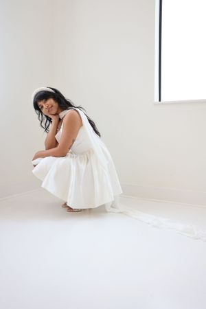 A white bridal portrait shows a crouching pose in a minimalist bright setting.