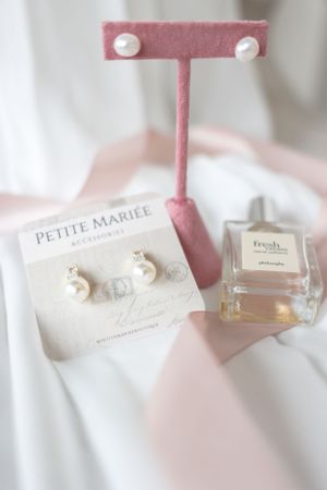 Pearl earrings, perfume and a pink jewelry stand arranged on white fabric with Petite Mariee branding.