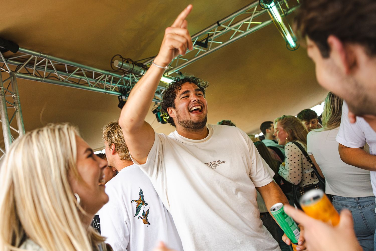 People dance and celebrate with arms raised under a tented event space ceiling during a lively party or celebration.