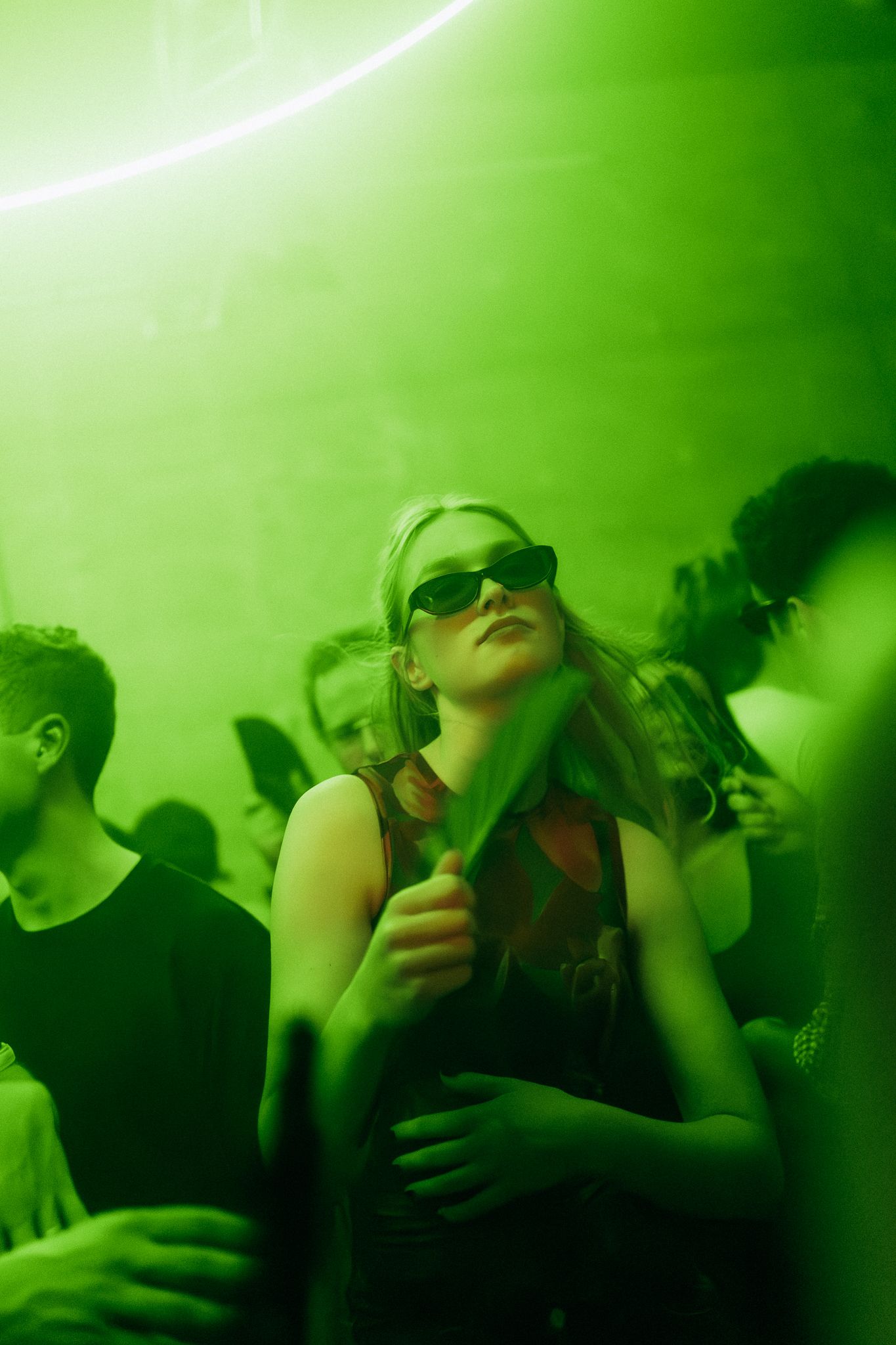 Crowd of people dancing in a nightclub bathed in green lighting during an energetic party atmosphere.