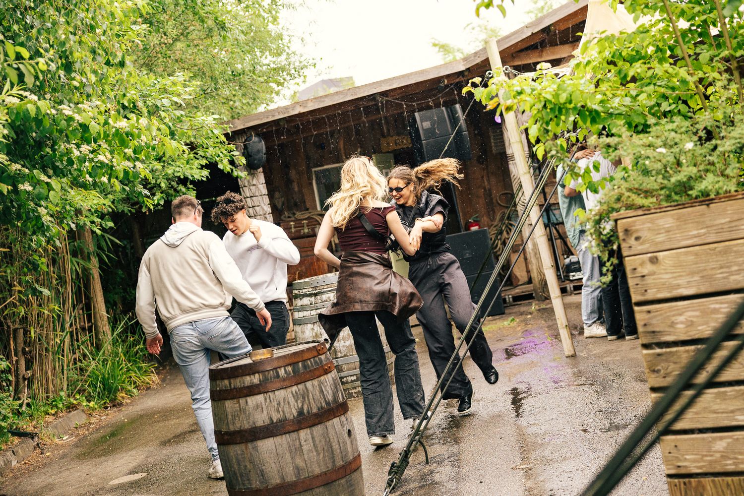 Three photographers balance on wooden barrels while taking pictures in a rustic outdoor setting.