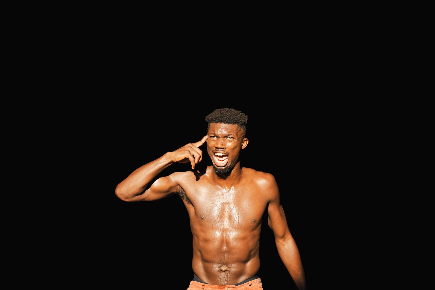 Shirtless muscular man smiling while talking on phone against black background.