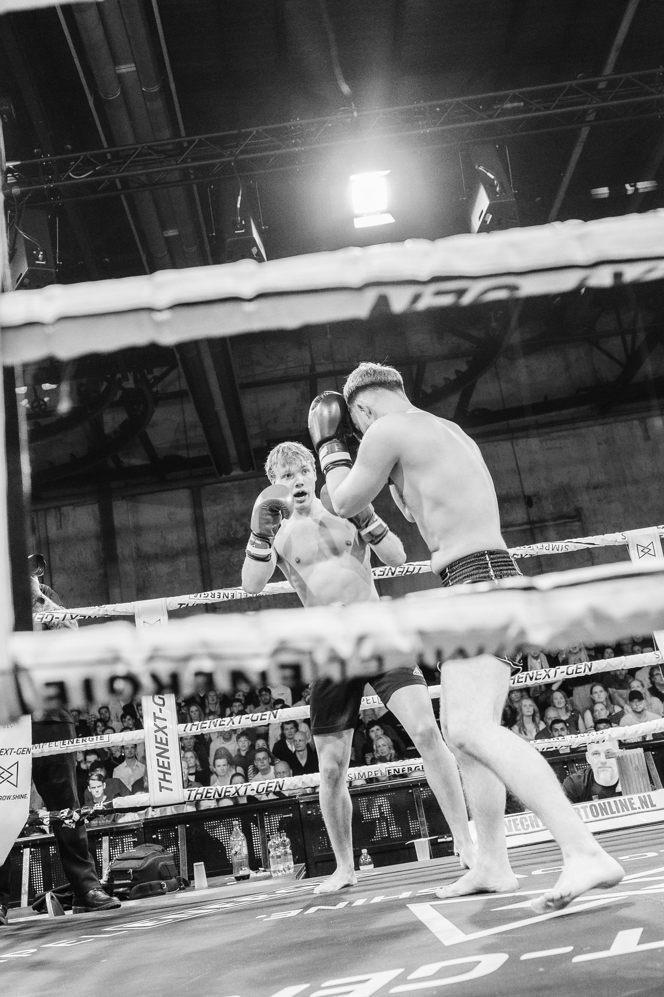 Two young male boxers sparring in a boxing ring during a competitive match, black and white photography.