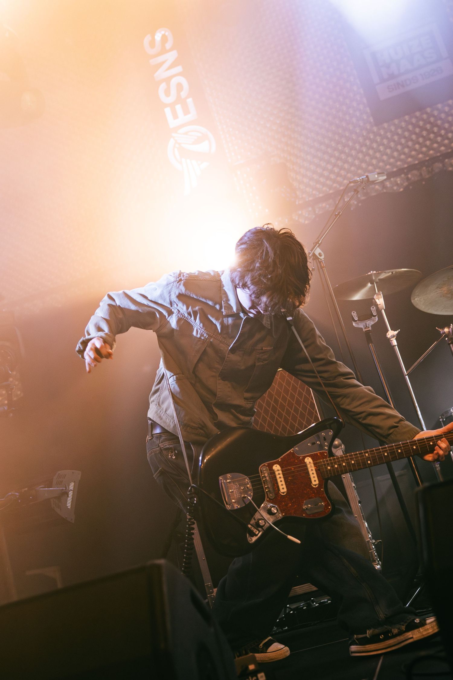 Guitarist performs on stage with dramatic orange backlighting creating a silhouetted effect during live concert performance.