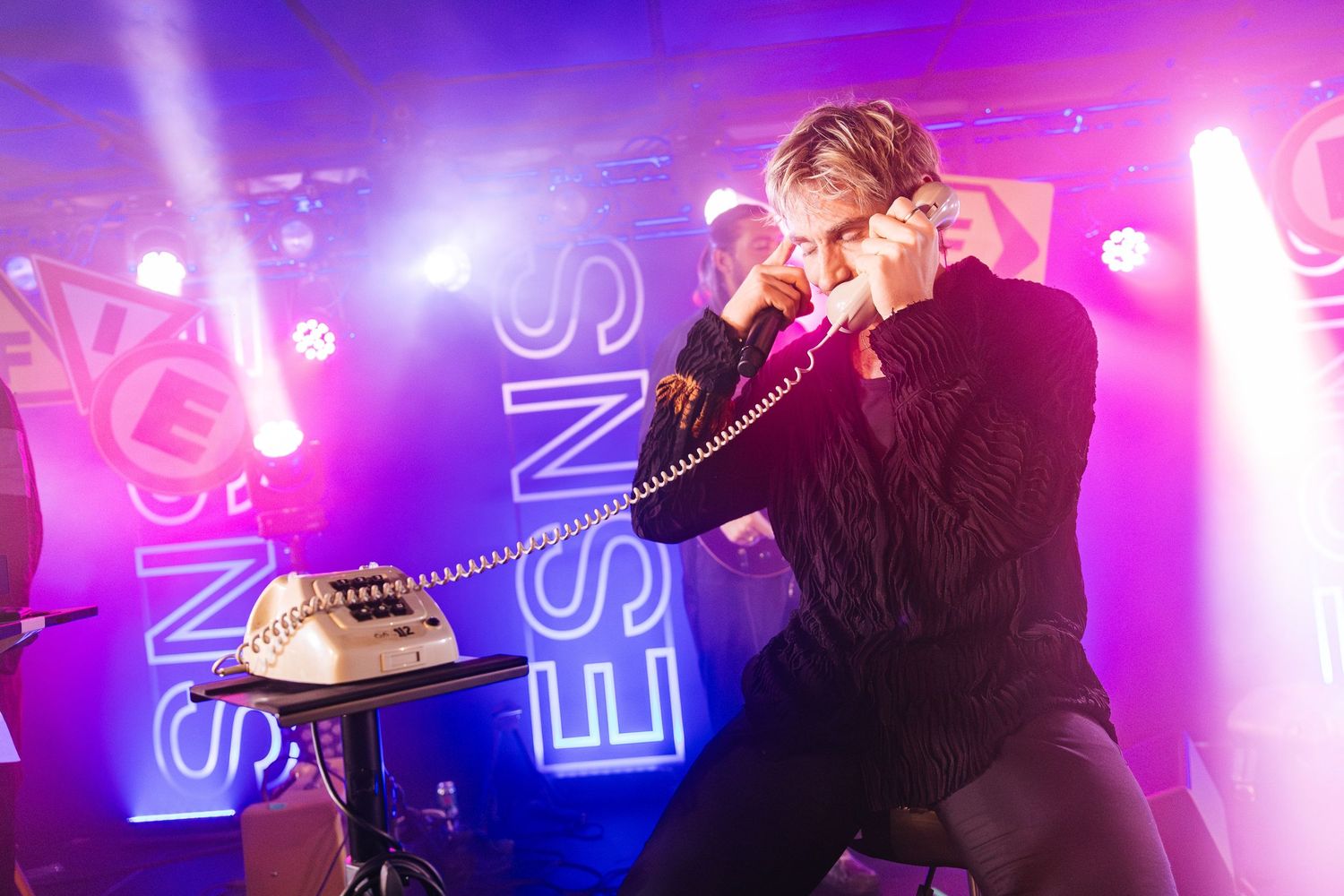 Concert performer silhouetted against vibrant purple and pink stage lighting during an energetic live music performance.