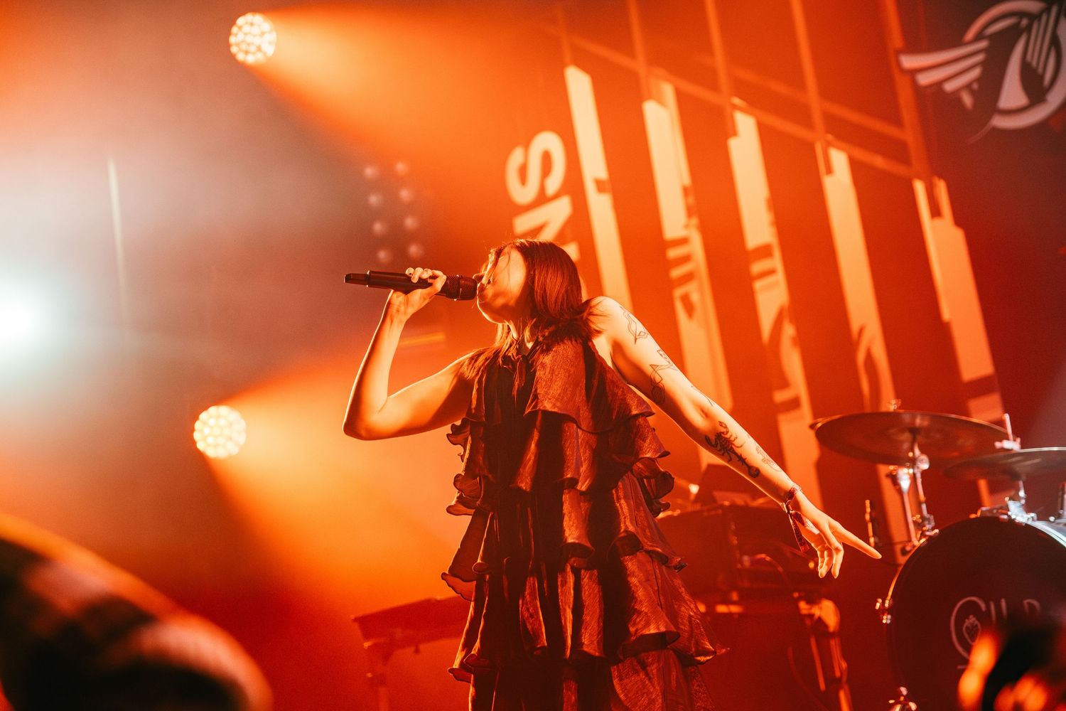 Concert performance with dramatic orange lighting and silhouetted figures on stage creating an atmospheric mood.
