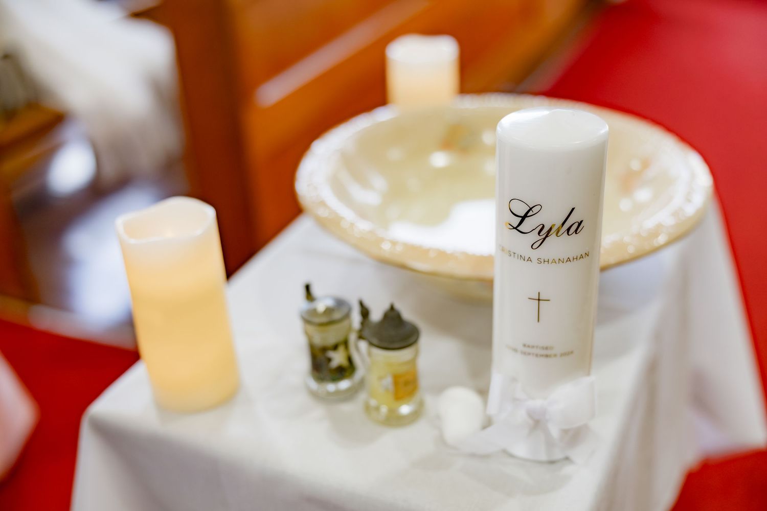 Baptism ceremony items including personalized candle and oils on white tablecloth.