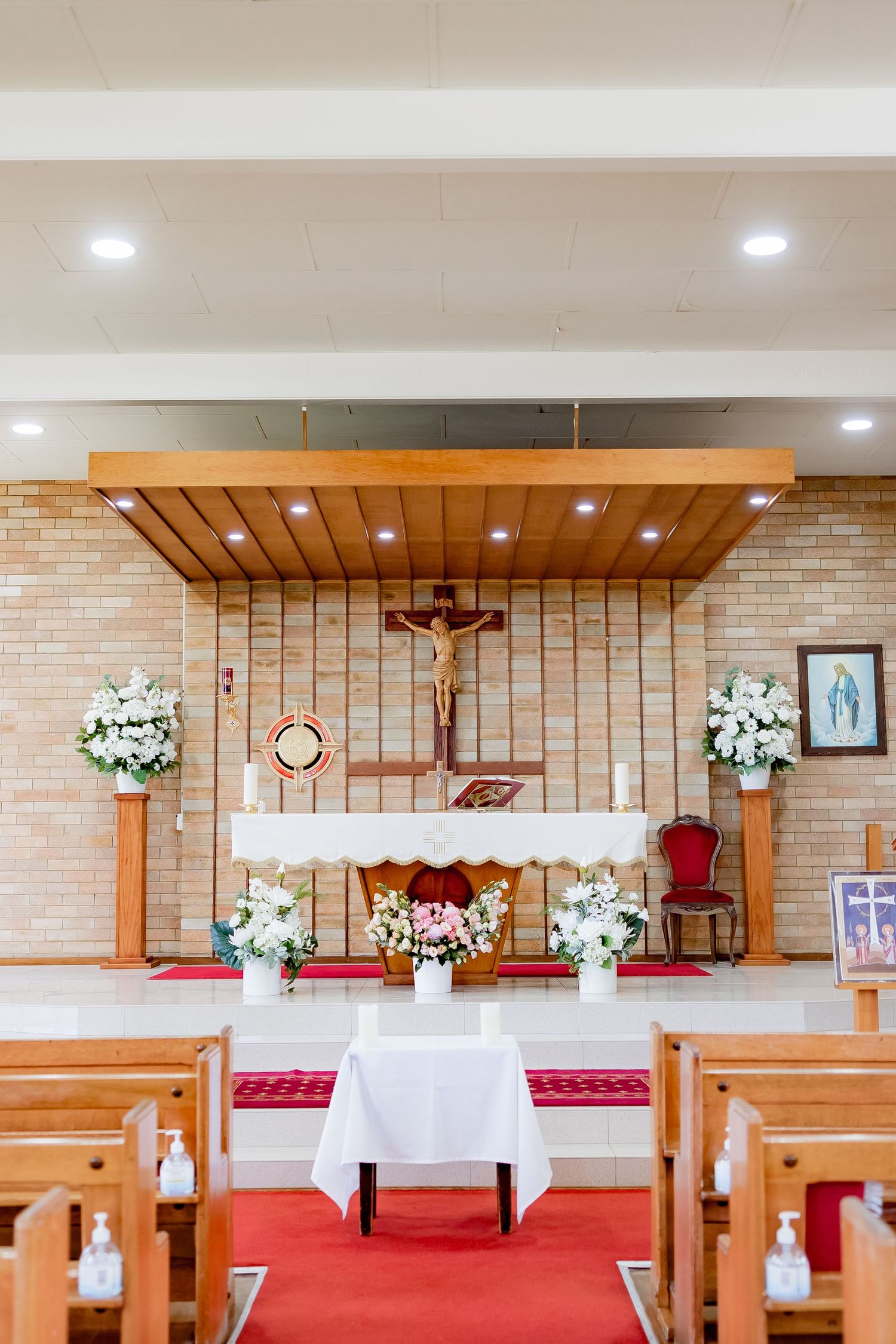 Church altar decorated with white floral arrangements and wooden pews for a ceremony.