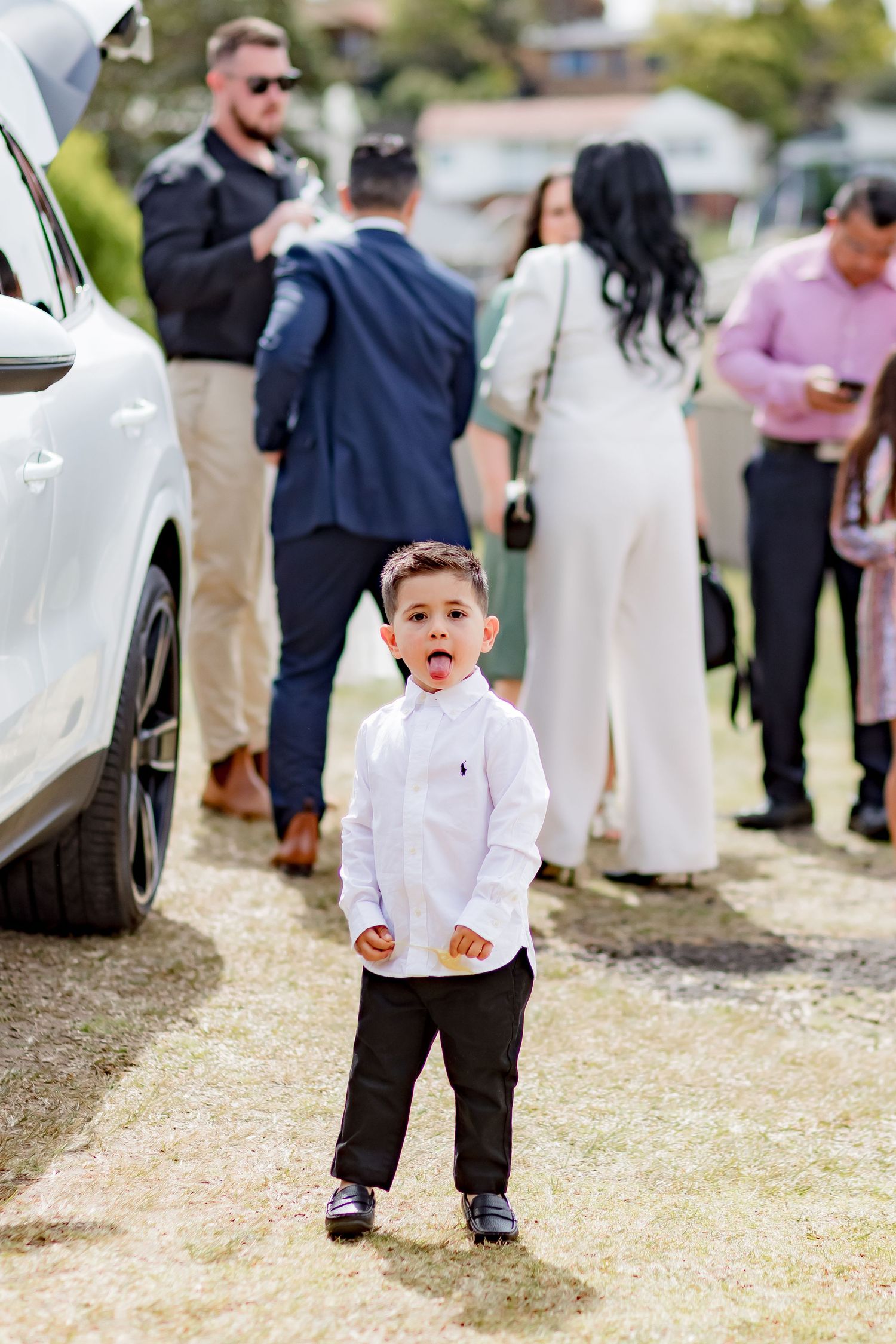 Young child in white shirt making an expressive face outdoors near a car.