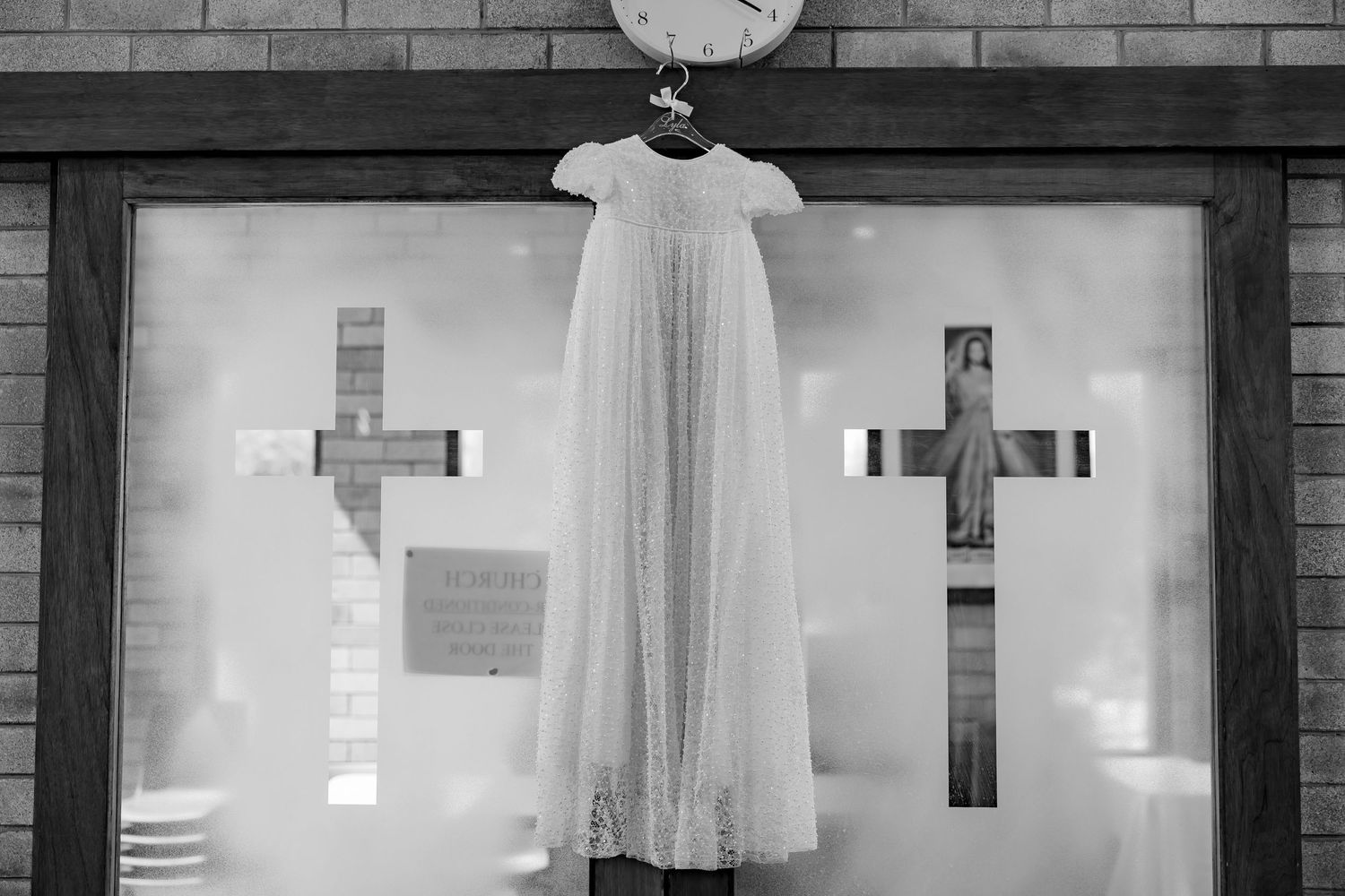 White baptismal or christening gown displayed against a brick wall with crosses.