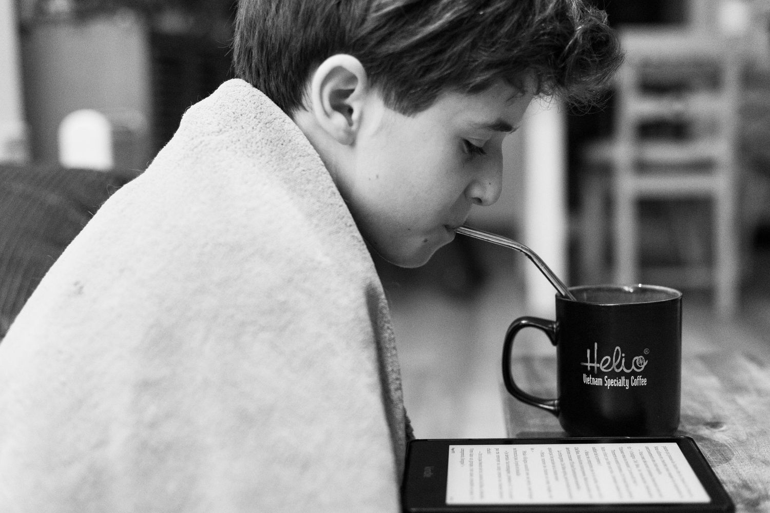 Person wrapped in blanket reading with coffee mug in black and white photography.