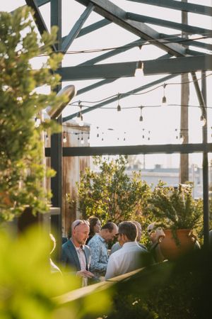 Wedding guests socializing under string lights in an outdoor covered venue.