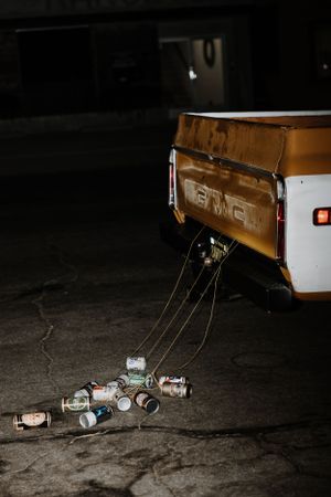 Empty beer cans and bottles scattered on dark ground next to a vehicle at night.