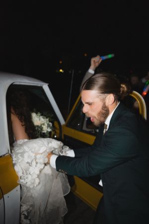 Wedding couple getting into a yellow taxi cab at night.