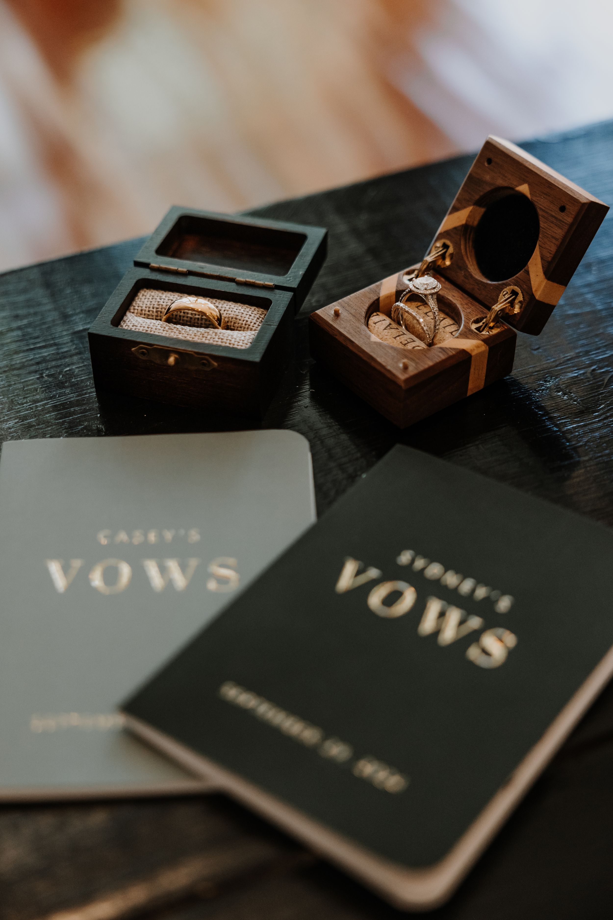 Wedding vow books and ring boxes arranged on dark surface.