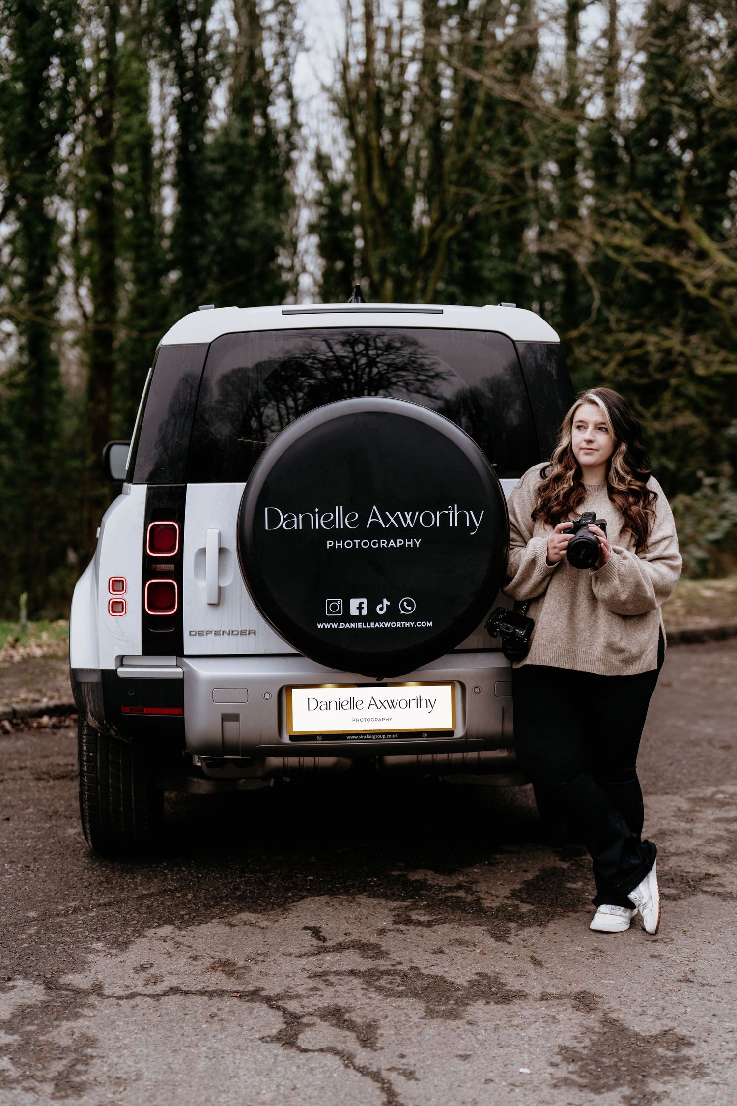 White Land Rover Defender with business branding parked in wooded area.