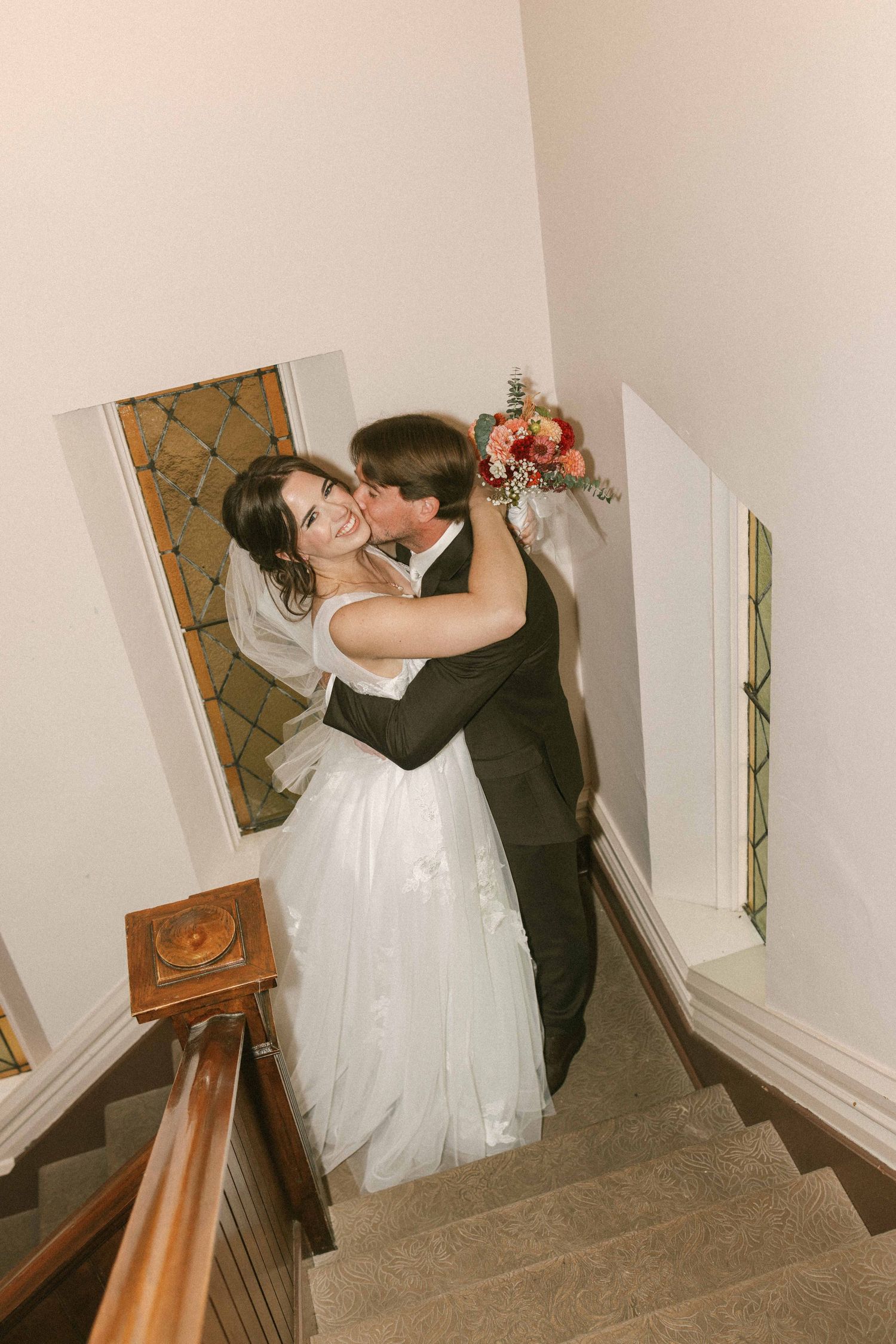 Sweet moment between newlyweds sharing a kiss on staircase with vintage decor.