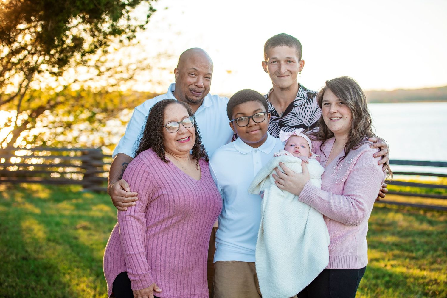 Multi-generational family portrait at sunset by a lakeside fence.