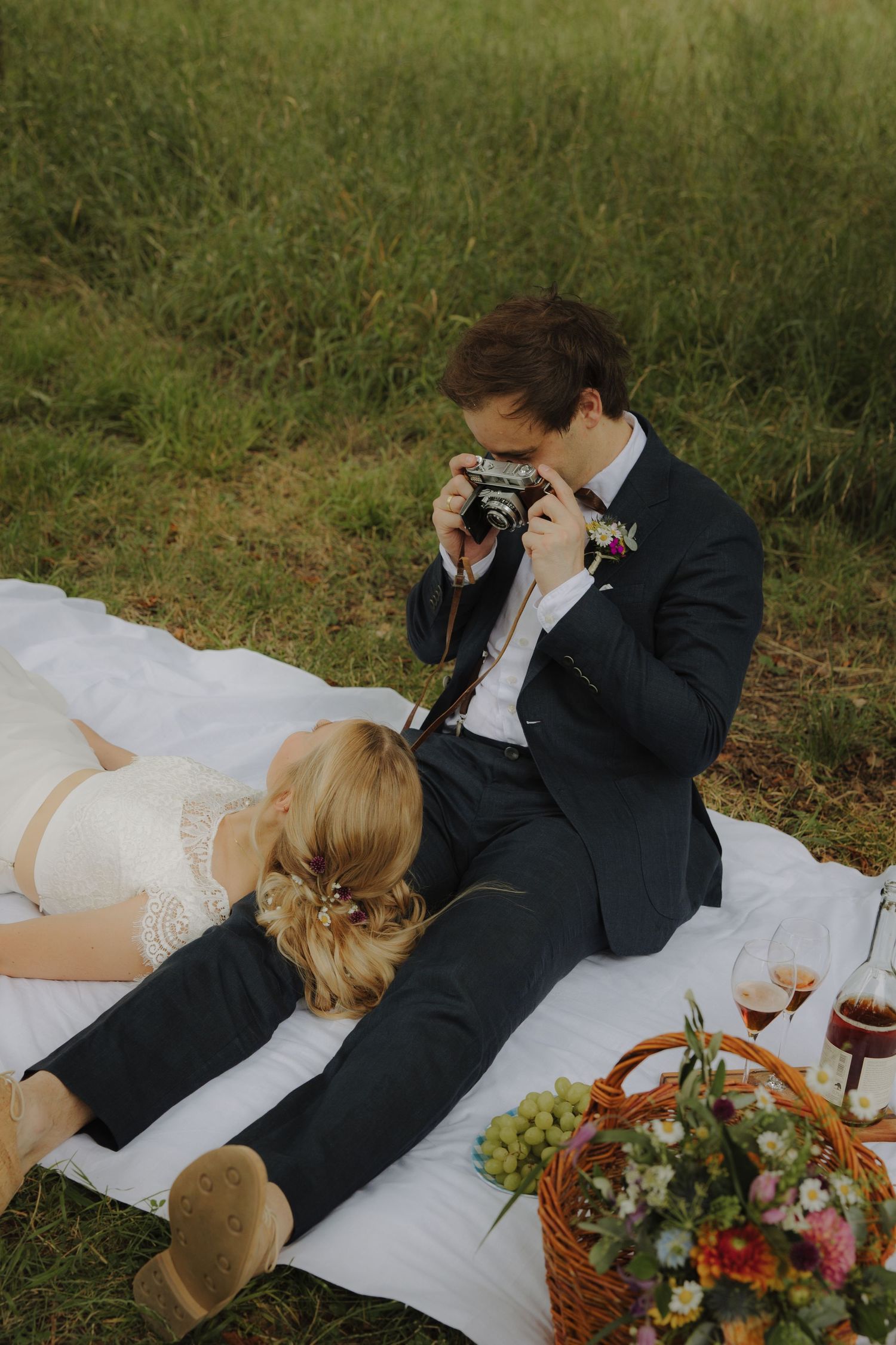 Couple enjoying intimate picnic moment with vintage camera and floral arrangements on white blanket.