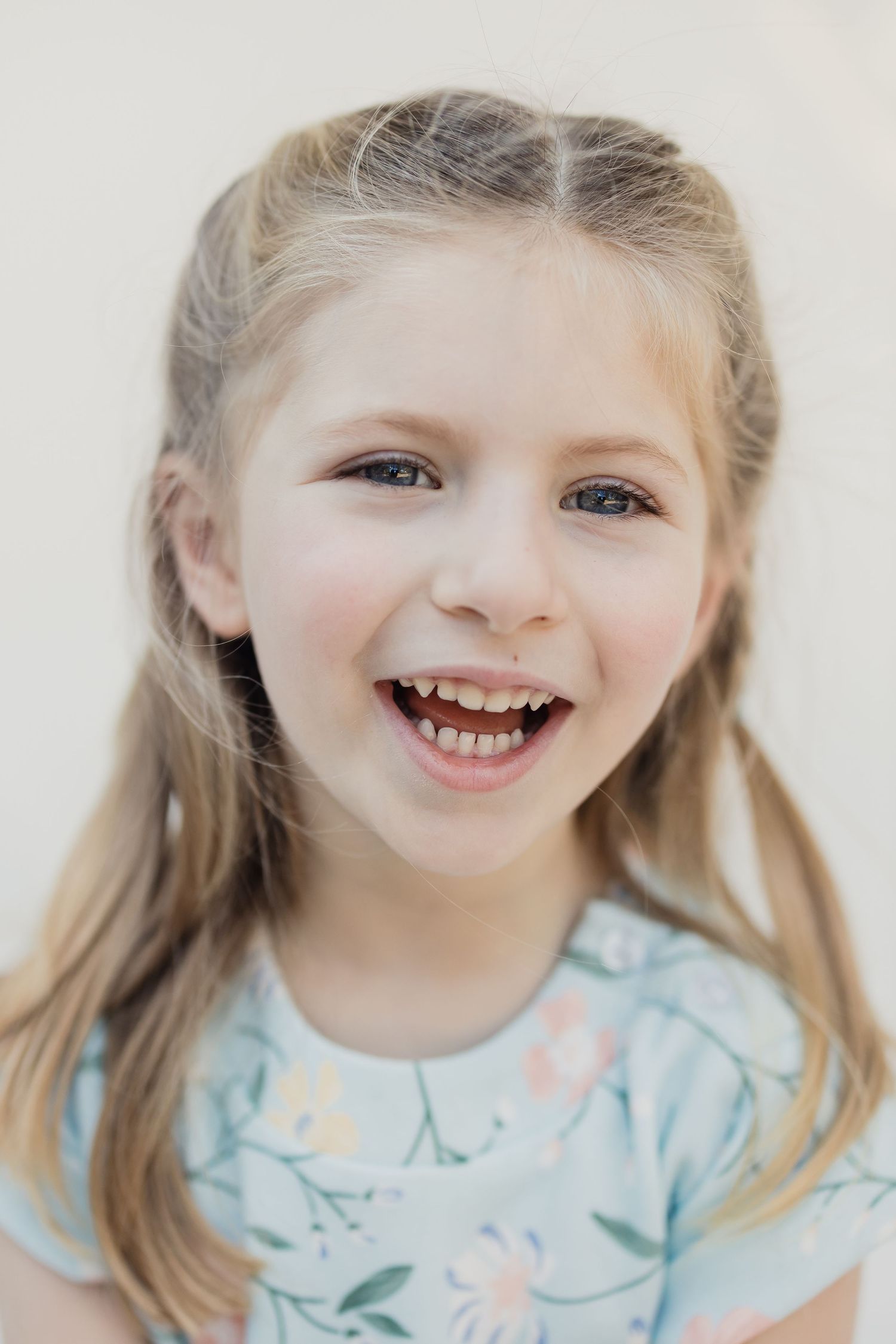 Portrait of young child with blonde hair wearing floral print shirt smiling brightly.