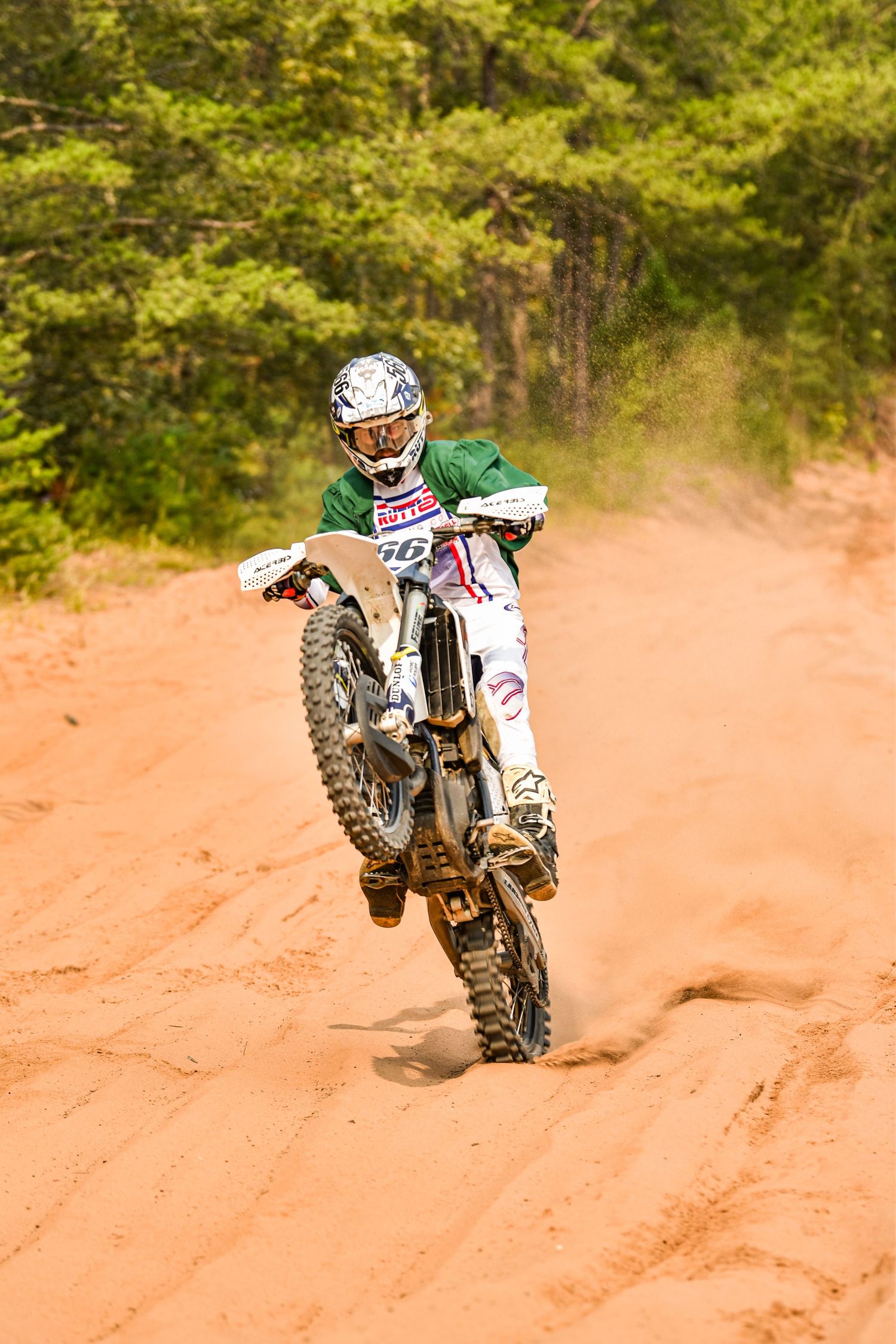 Motocross rider in full gear racing through a dusty dirt track in wooded area.