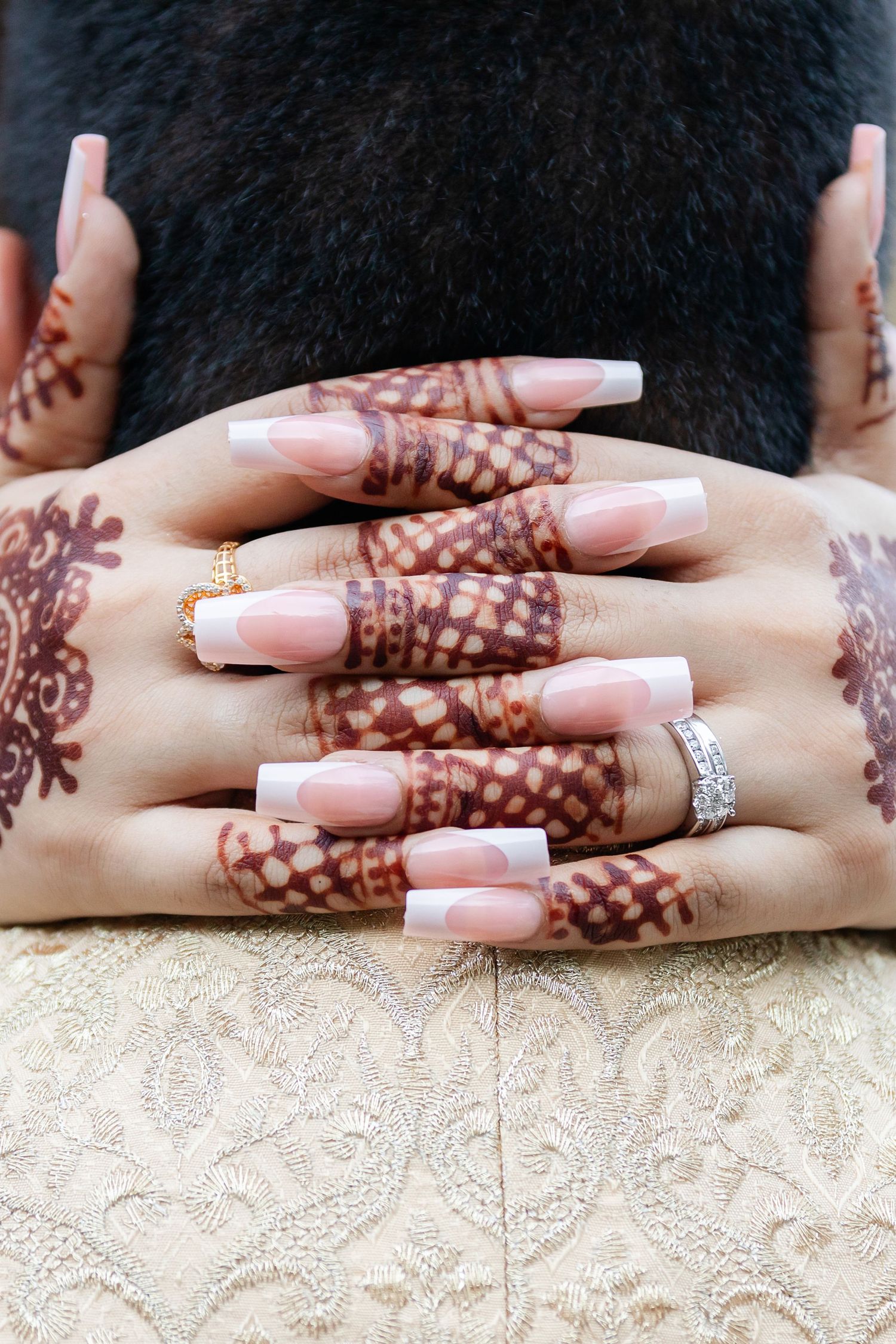 Detailed henna designs on hands with pink manicure and engagement ring.