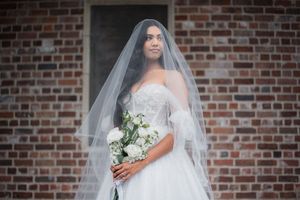 Bridal portraits against rustic brick wall featuring white floral bouquet and flowing veil.