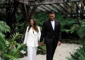 Couple walking through garden path surrounded by lush greenery and trees.