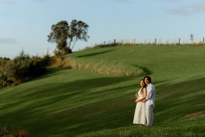 Couple embracing on a rolling green golf course with a lone tree on the hilltop at sunset.