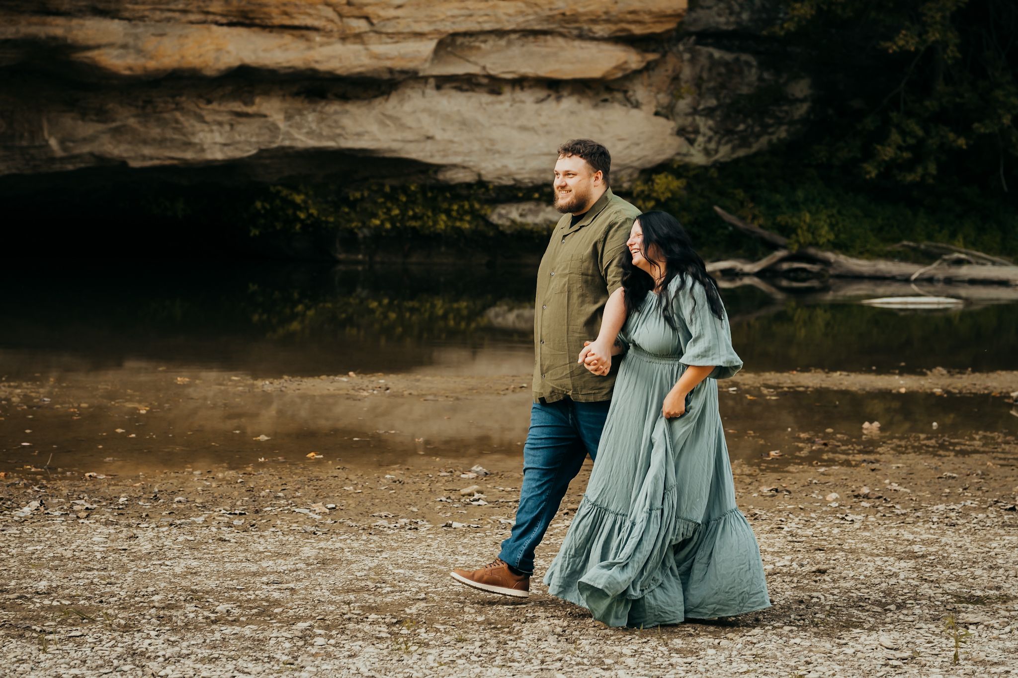 A couple in casual attire poses against a rocky cliff backdrop during an outdoor photoshoot.
