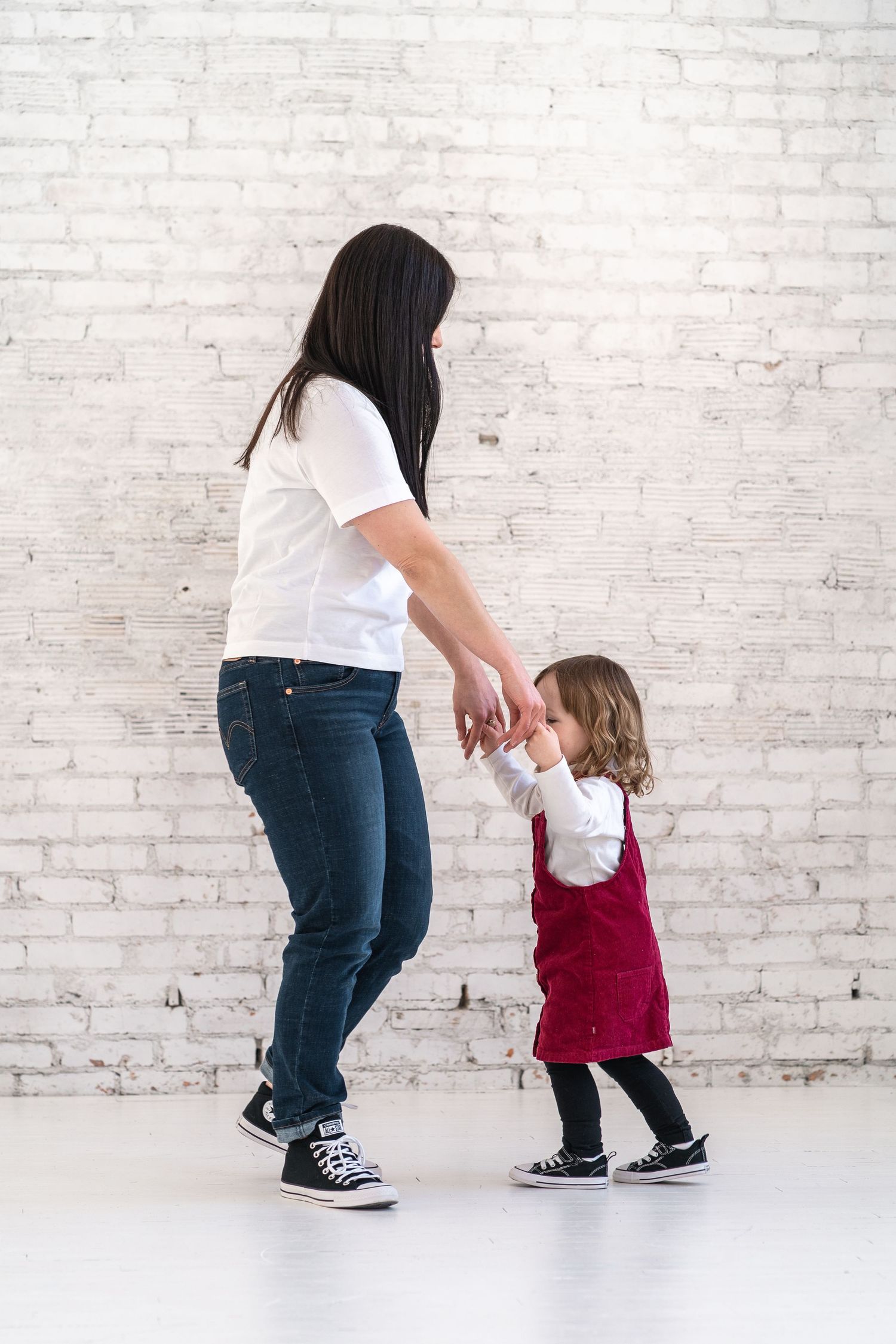 Dancing together in casual outfits against white brick wall background.