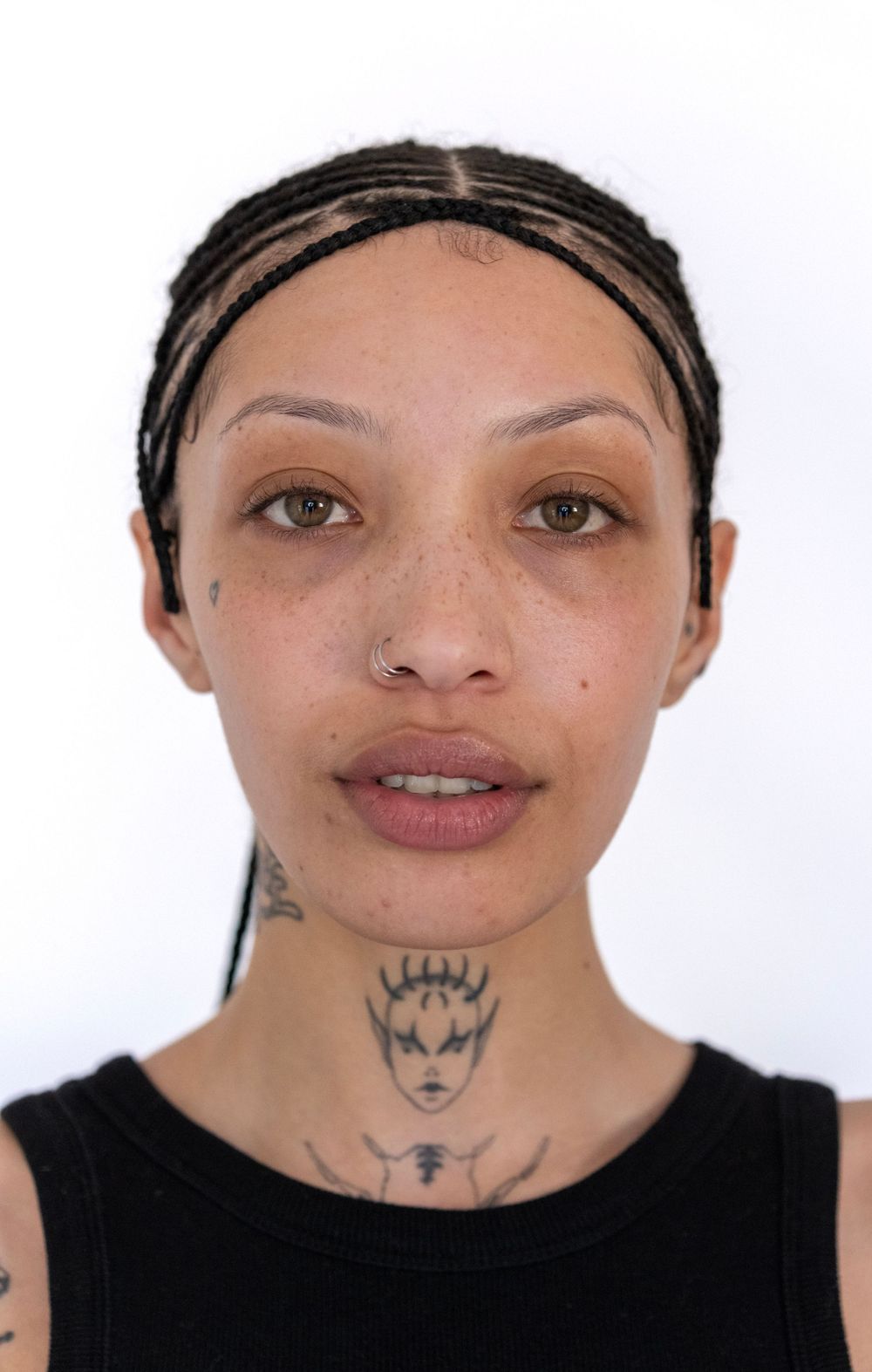 Model with braided hair and neck tattoo poses in black tank top against white background.