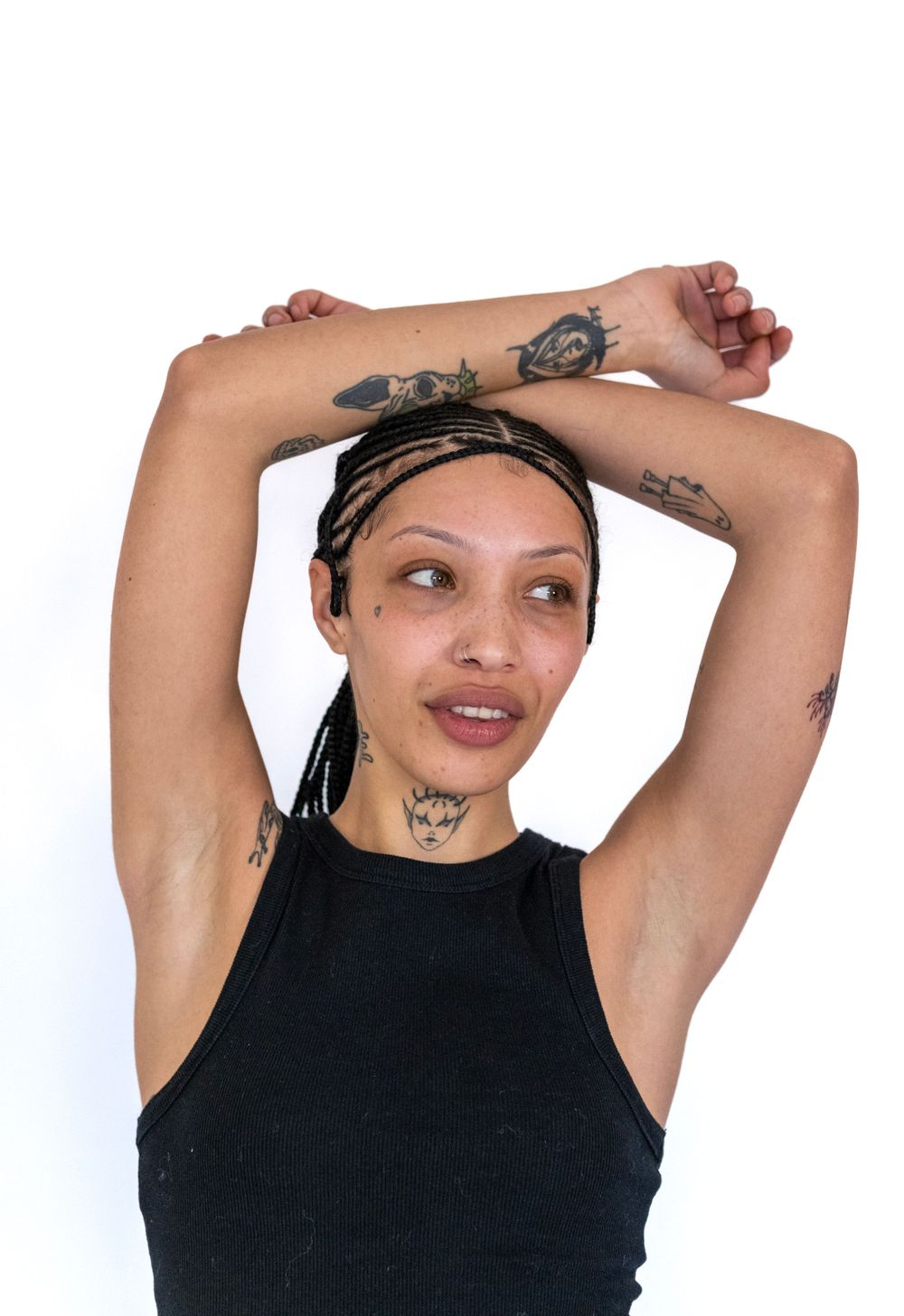 Fashion portrait showcasing multiple arm tattoos and braided hairstyle with black tank top.