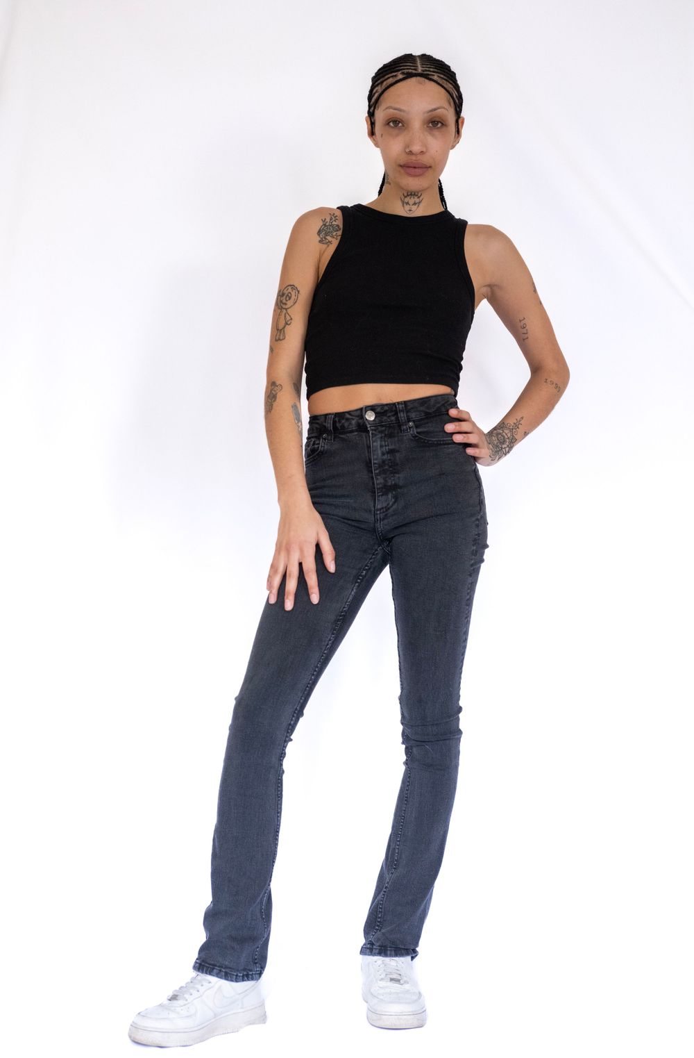 Full body fashion shot in black crop top and jeans with white sneakers.