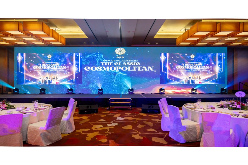 Elegant ballroom event setup with large digital screens displaying blue graphics and white chair covers in a luxurious venue.