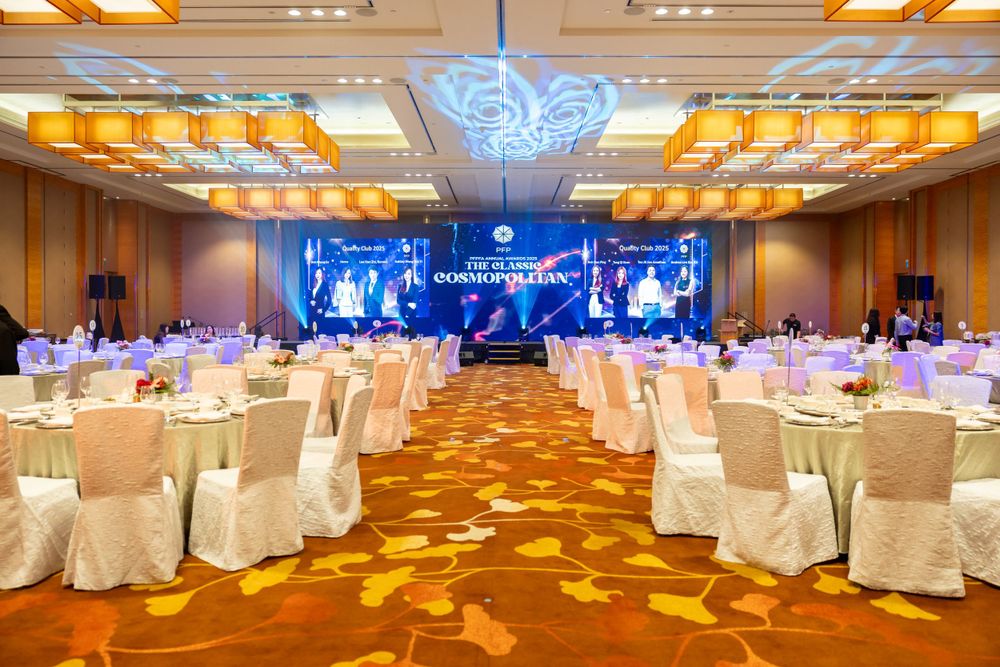 Elegant banquet hall setup with white chair covers, golden carpet and blue lighting on stage for formal event.
