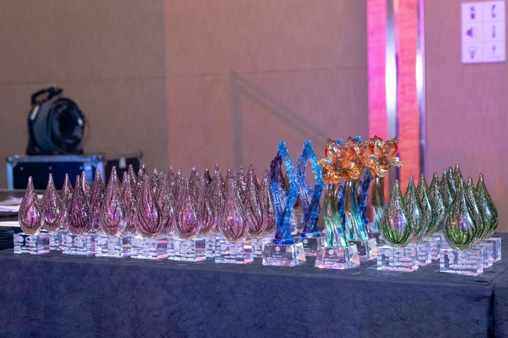 Colorful glass trophies and awards arranged on a dark display table with pink ambient lighting in the background.