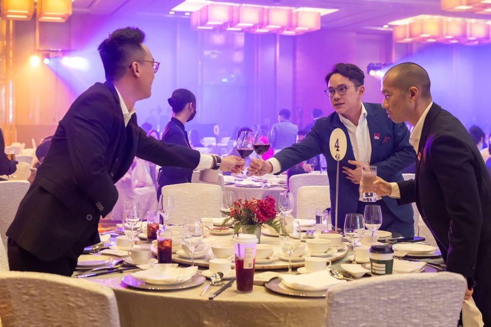 People engaged in conversation at an elegant dinner event with purple mood lighting and formal table settings.