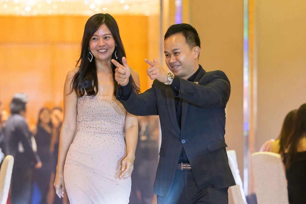 A couple in formal attire dances together at an elegant event with soft orange lighting in the background.