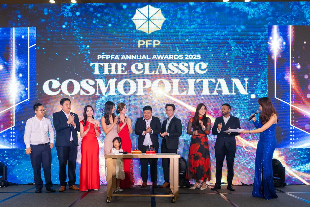Large group photo at an elegant corporate event with blue lighting and 'THE CLASSIC COSMOPOLITAN' text display on stage.